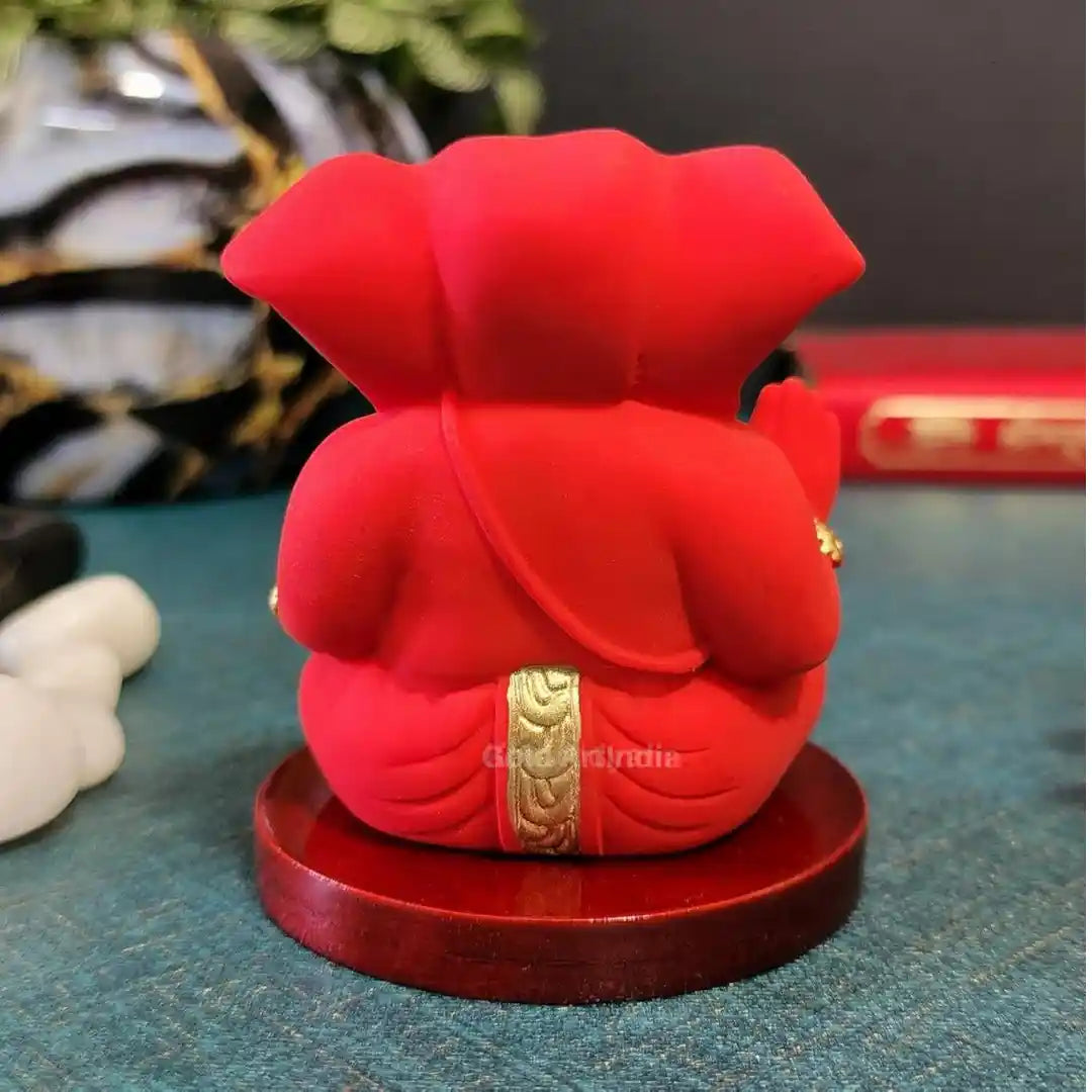 Rear view of handcrafted red Ganesha idol with golden detailing on wooden base