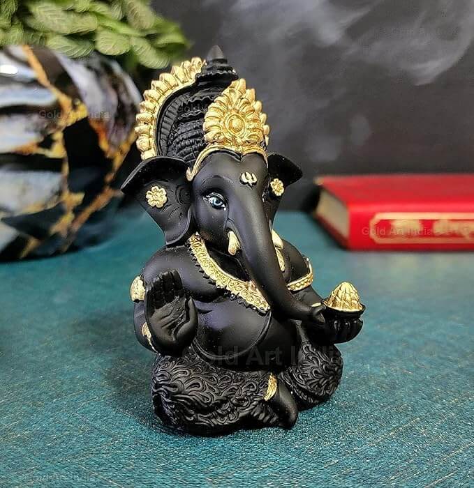 mango terracotta Ganesha idol with Gold detailing, seated in a blessing posture, holding a modak in one hand.