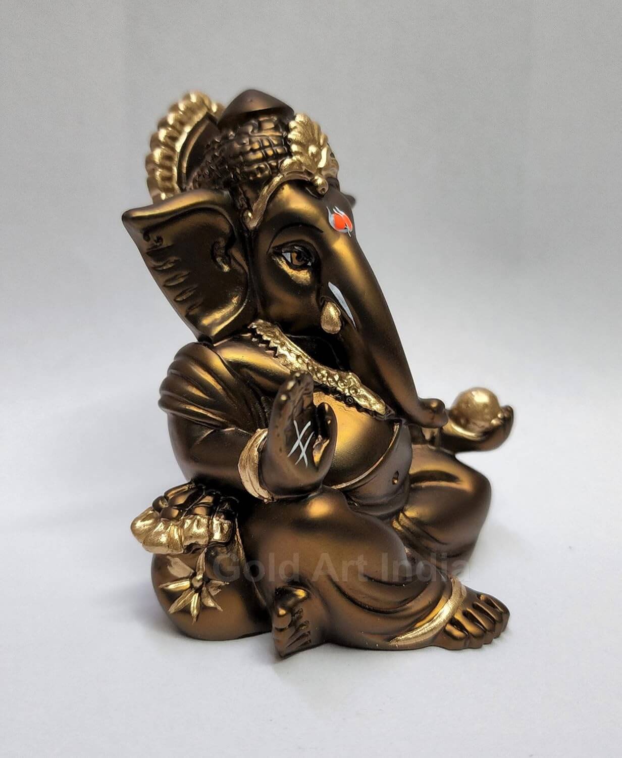 A 3.5-inch bronze-colored Ganesha statue with a crown, jewelry, and intricate carvings. One hand gives blessings, the other holds a golden Ladoo.