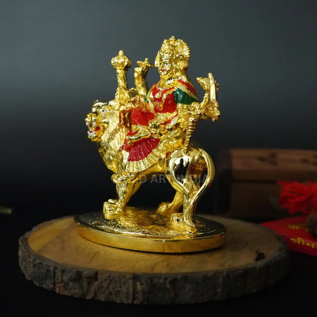 Angled side profile of handcrafted Gold Plated Ambe Idol with red enamel clothing, seated on lion