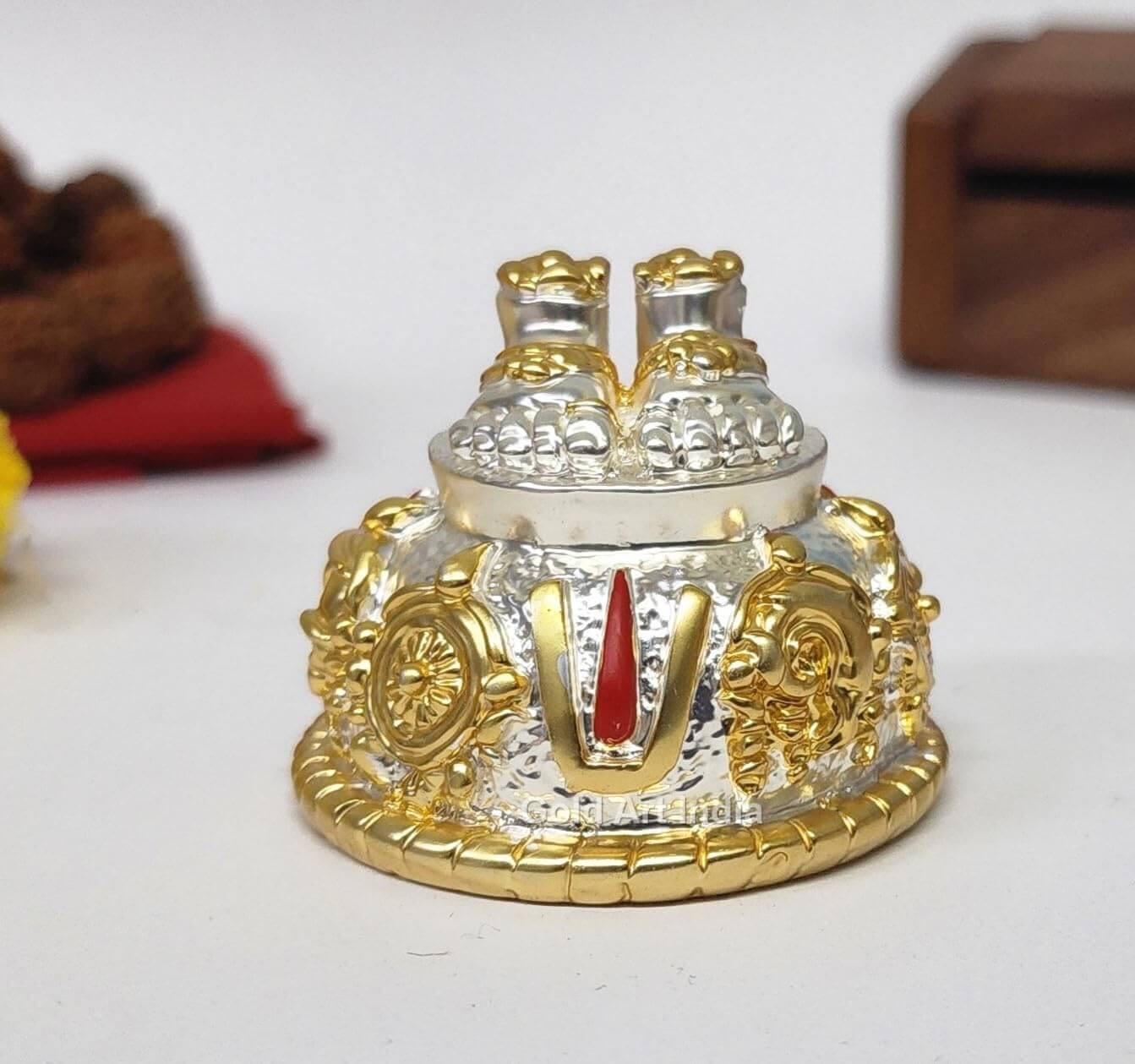 A silver and gold decorative idol featuring Lord Balaji's feet (Paduka) with intricate carvings of religious symbols and ornaments.