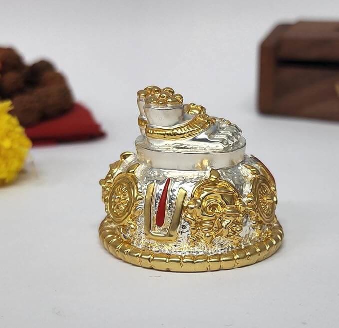 A silver and gold decorative idol featuring Lord Balaji's feet (Paduka) with intricate carvings of religious symbols and ornaments.