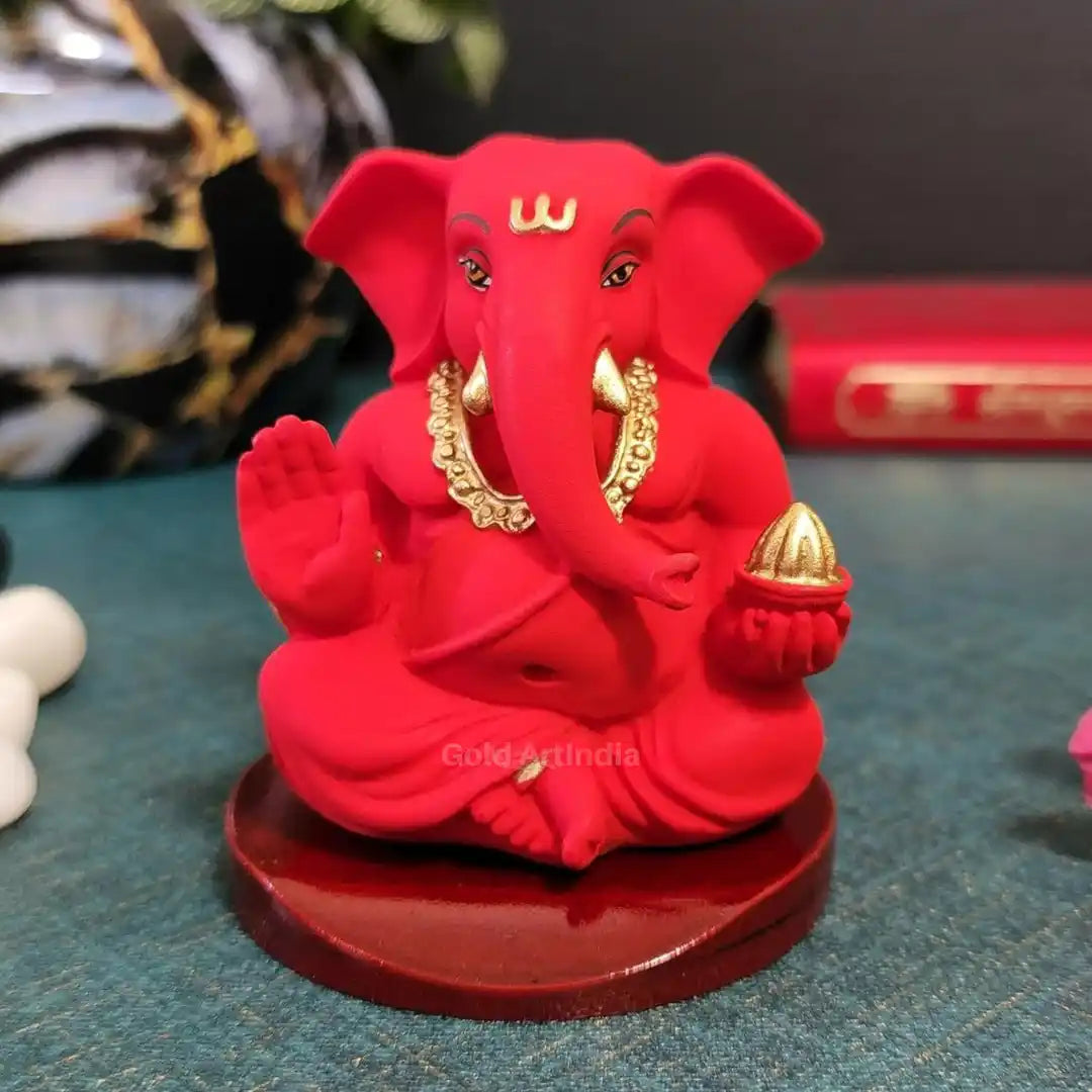 Handcrafted red Ganesha idol with golden detailing, seated on a round wooden base – front view