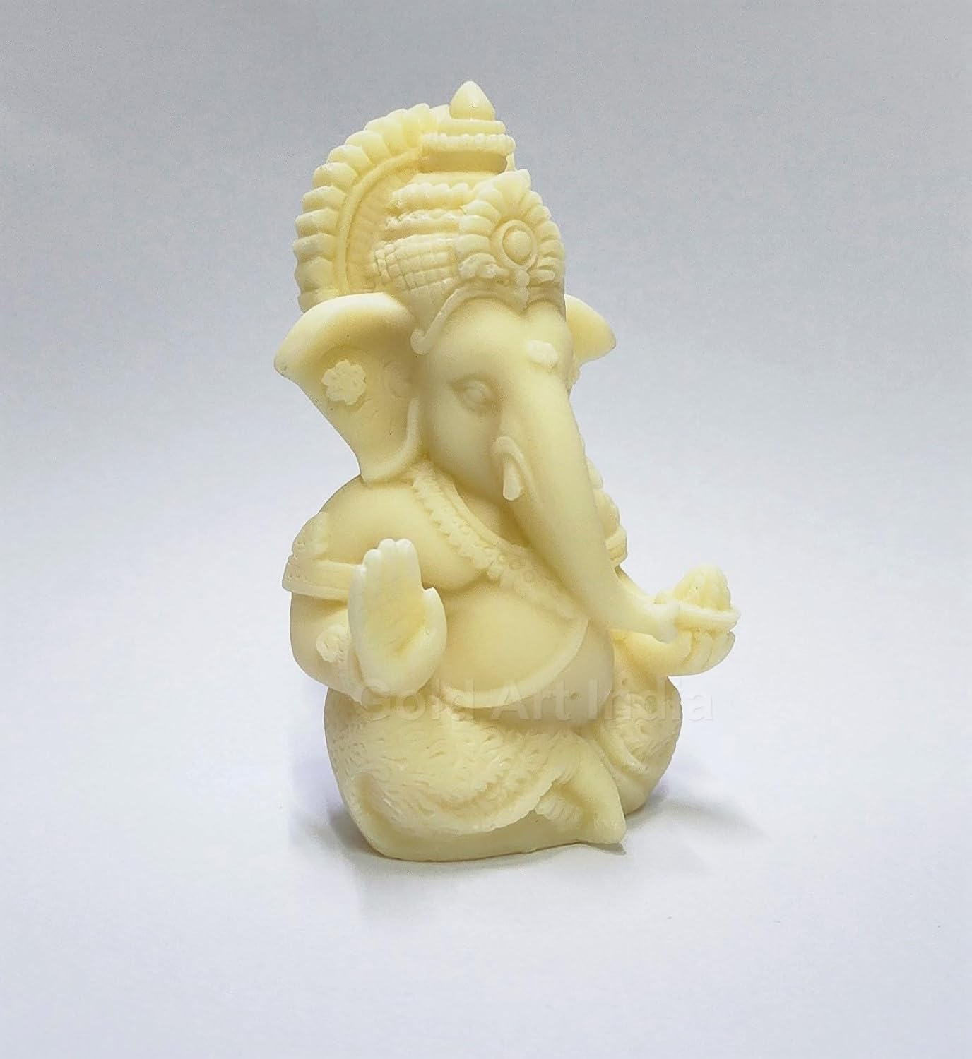 A 3.5-inch Ivory_Finish Ganesha statue with a crown, jewelry, and intricate carvings. One hand gives blessings, the other holds a modak. side view