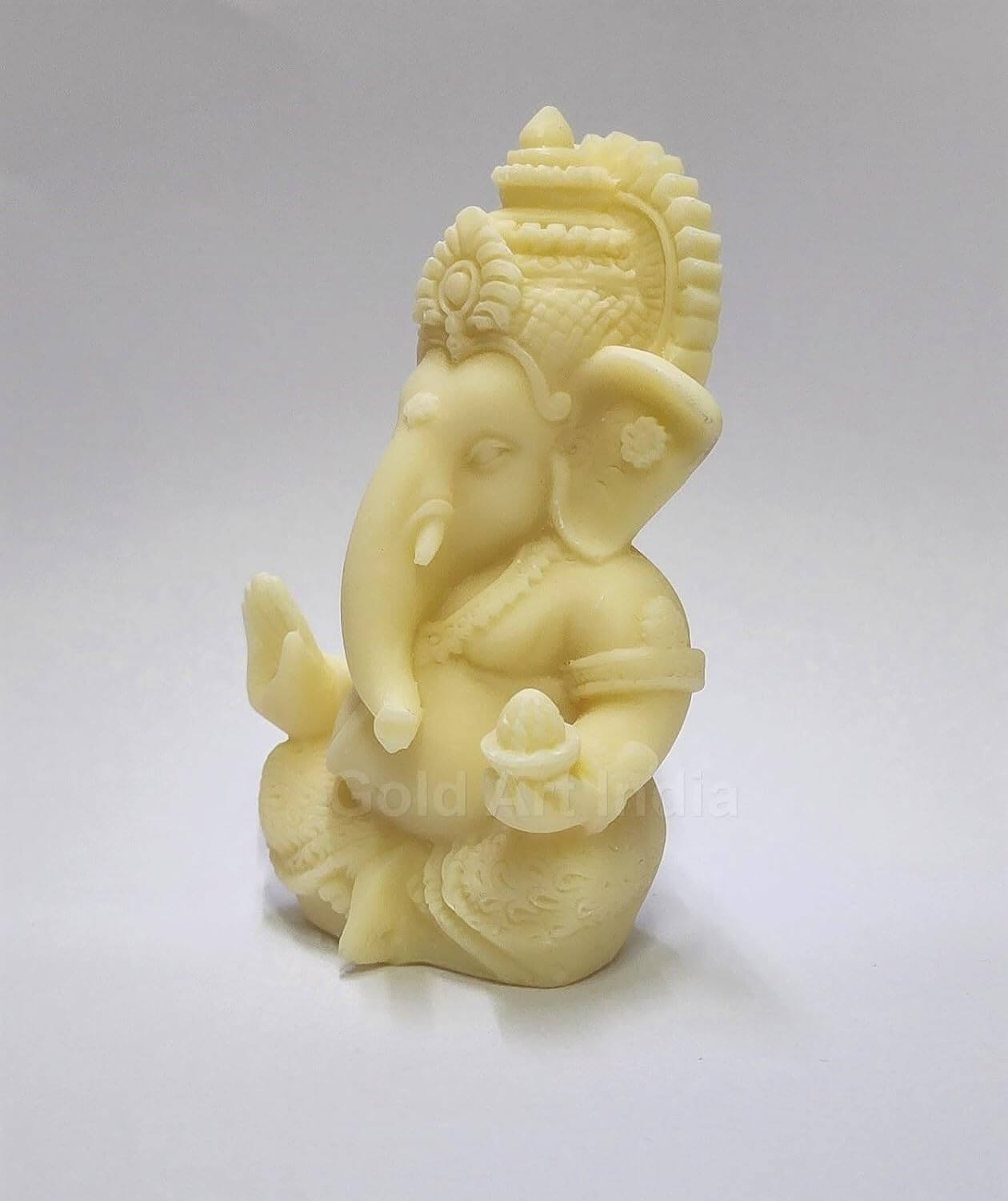 A 3.5-inch Ivory_Finish Ganesha statue with a crown, jewelry, and intricate carvings. One hand gives blessings, the other holds a modak. side view