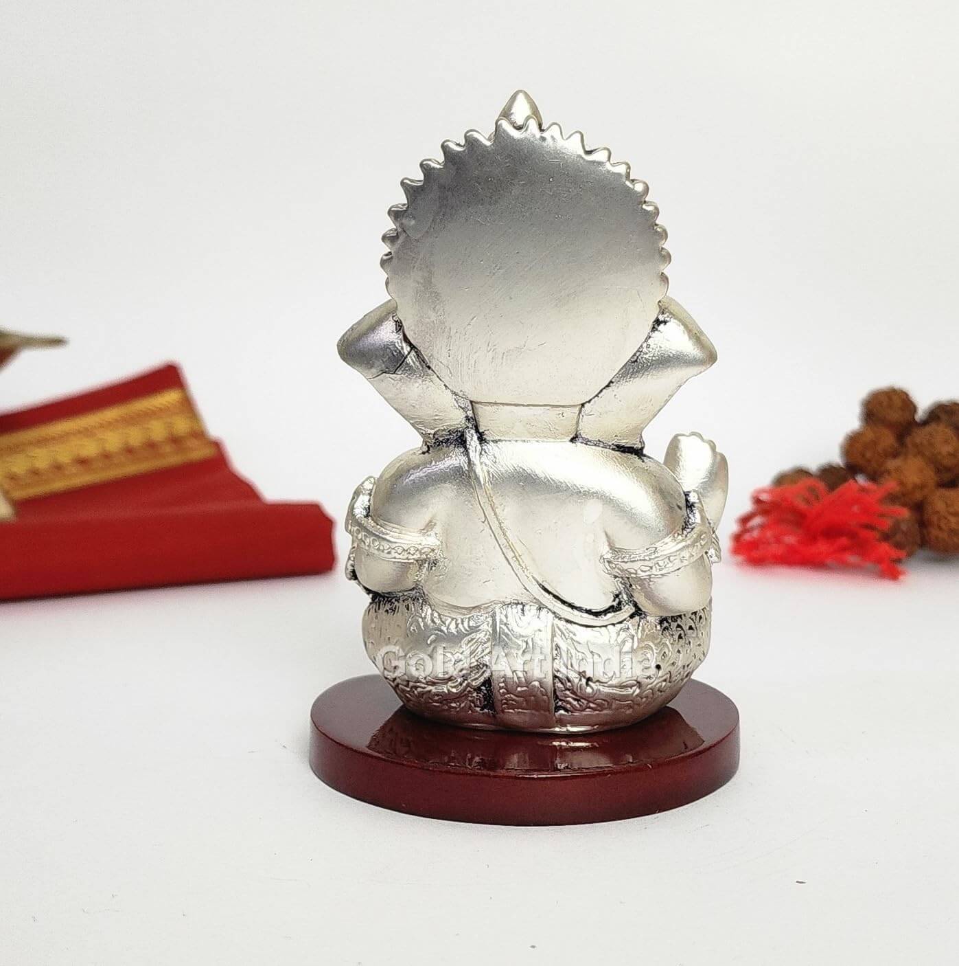 A 3.5-inch Silver Plated Antique Finish Mdf base Ganesha statue with a crown, jewelry, and intricate carvings. Decorated with Rudraksh and red cloth in the background. back view