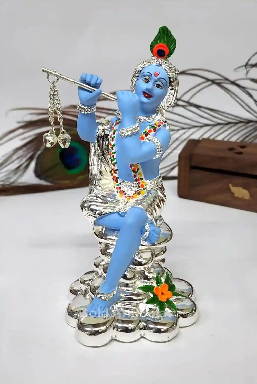 "A silver-Plated statue of Lord Krishna playing the flute, adorned with a peacock feather and colorful jewelry."