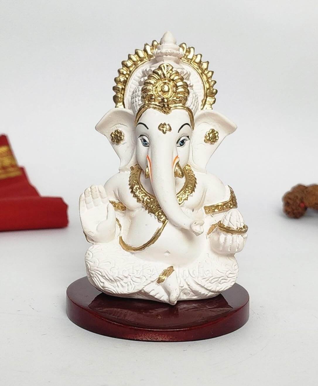 A 3.5-inch Peach Ivory Mdf base Ganesha statue with a crown, jewelry, and intricate carvings. One hand gives blessings, the other holds a modak. Decorated with Rudraksh and red cloth in the background.