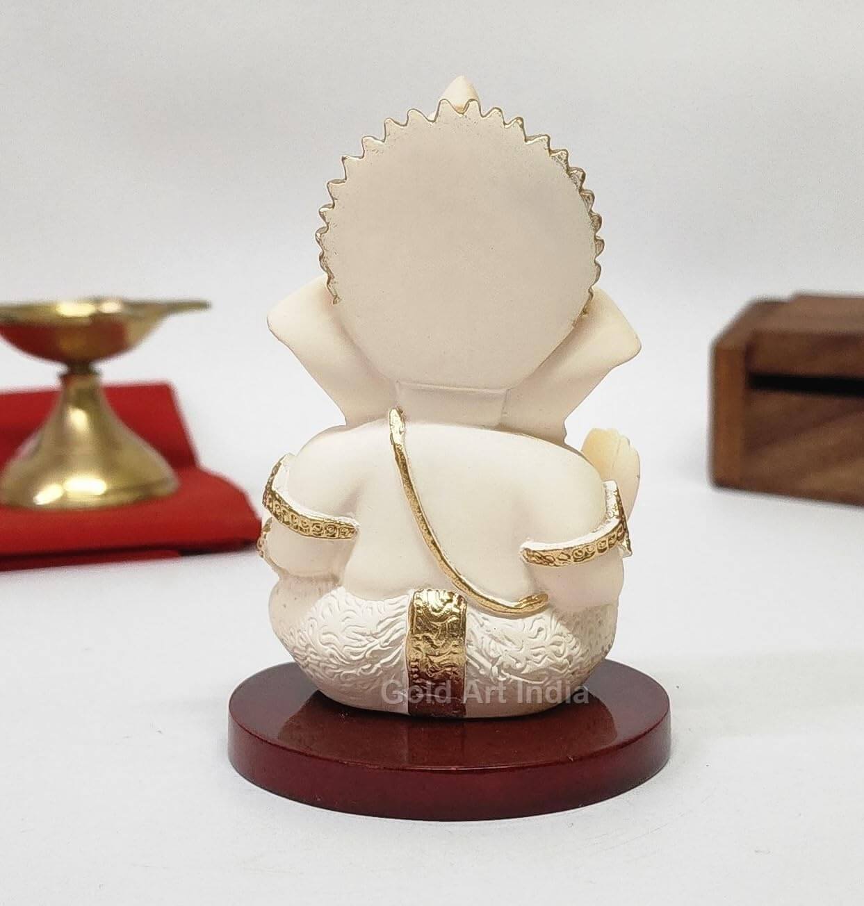 A 3.5-inch Peach Ivory Mdf base Ganesha statue with a crown, jewelry, and intricate carvings. ack view Decorated with box and red cloth in the background.