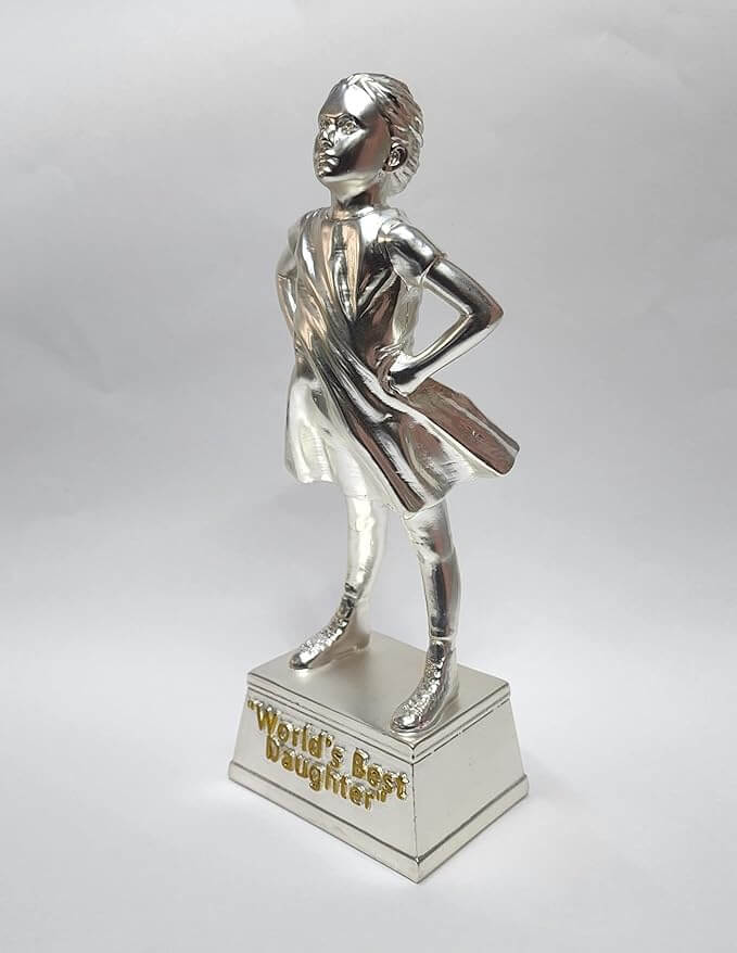 A silver-plated trophy of a confident young girl standing with her hands on her hips. The figure is fully silver, with a flowing dress and ponytail. The trophy stands on a rectangular silver base with the engraved text "World's Best Daughter" .