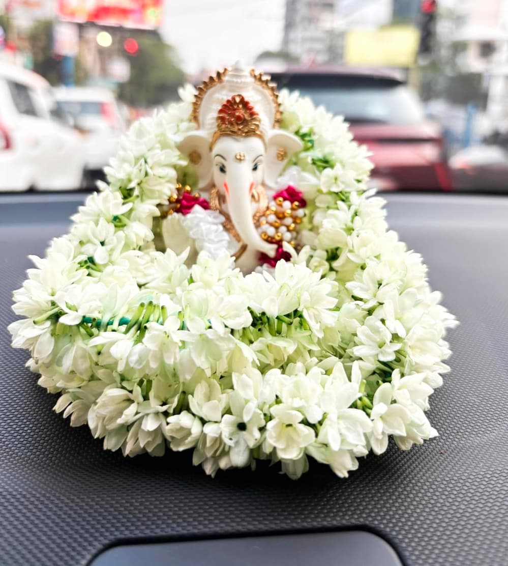 Gold and red-crowned Ganesha idol on car dashboard with white jasmine garland – symbol of divine protection and purity during travel