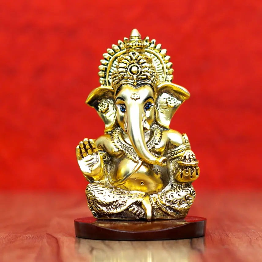 Gold-plated Lord Ganesha idol with intricate detailing, seated on a wooden base against a red background