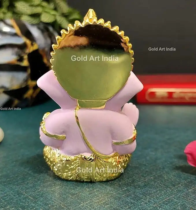 Backview of a white and gold Lord Ganesha idol with intricate detailing, a blessing hand, and a modak in the other.