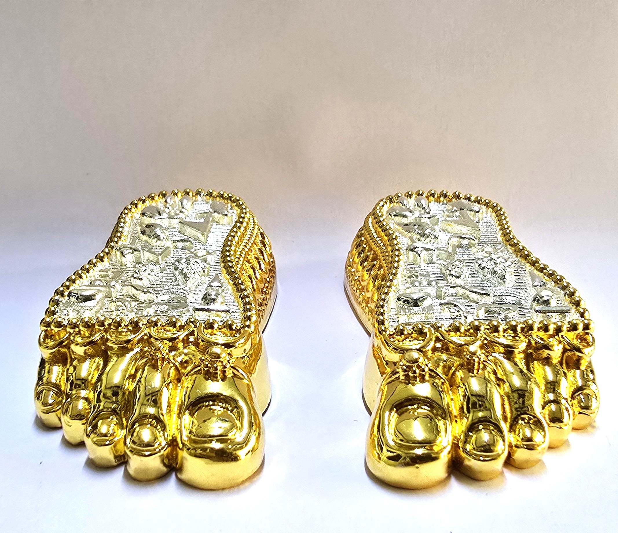 Gold and silver plated Charan Paduka with intricate symbols and embossed design, placed in front of a wooden stand.