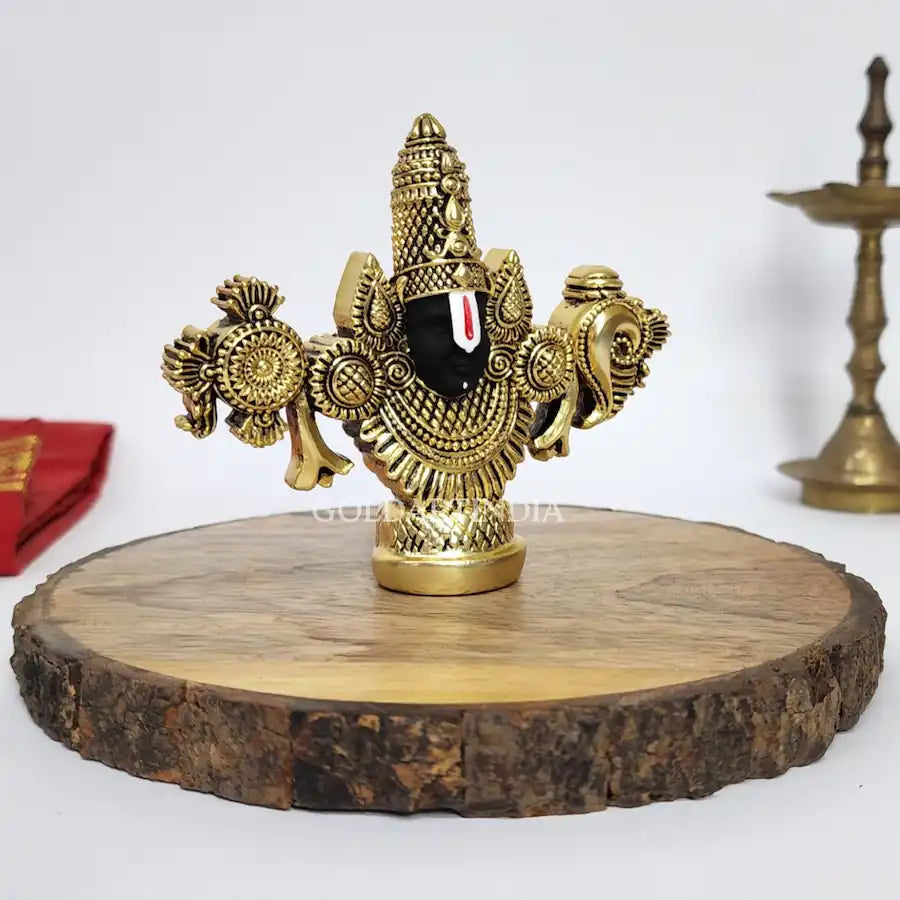 Gold-plated Lord Balaji idol with black face on wooden base.