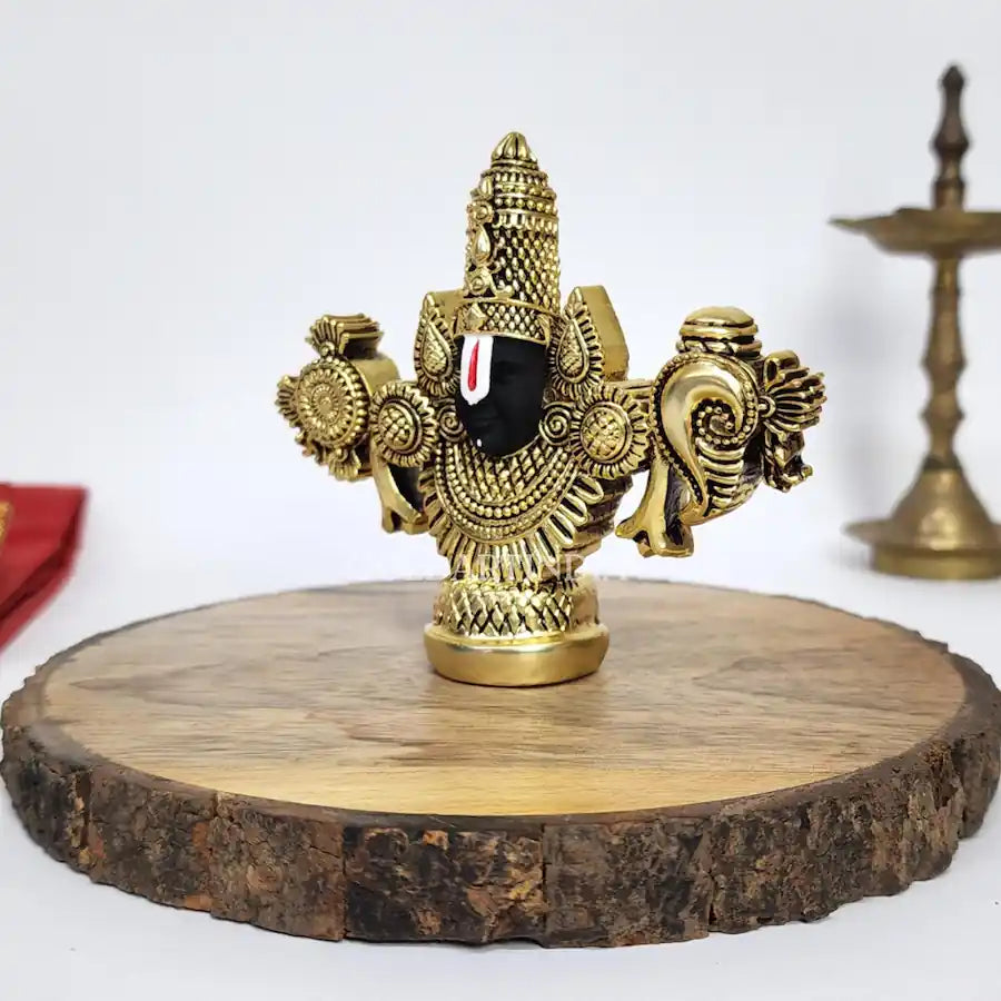 Gold-plated Lord Balaji idol with black face on wooden base.
