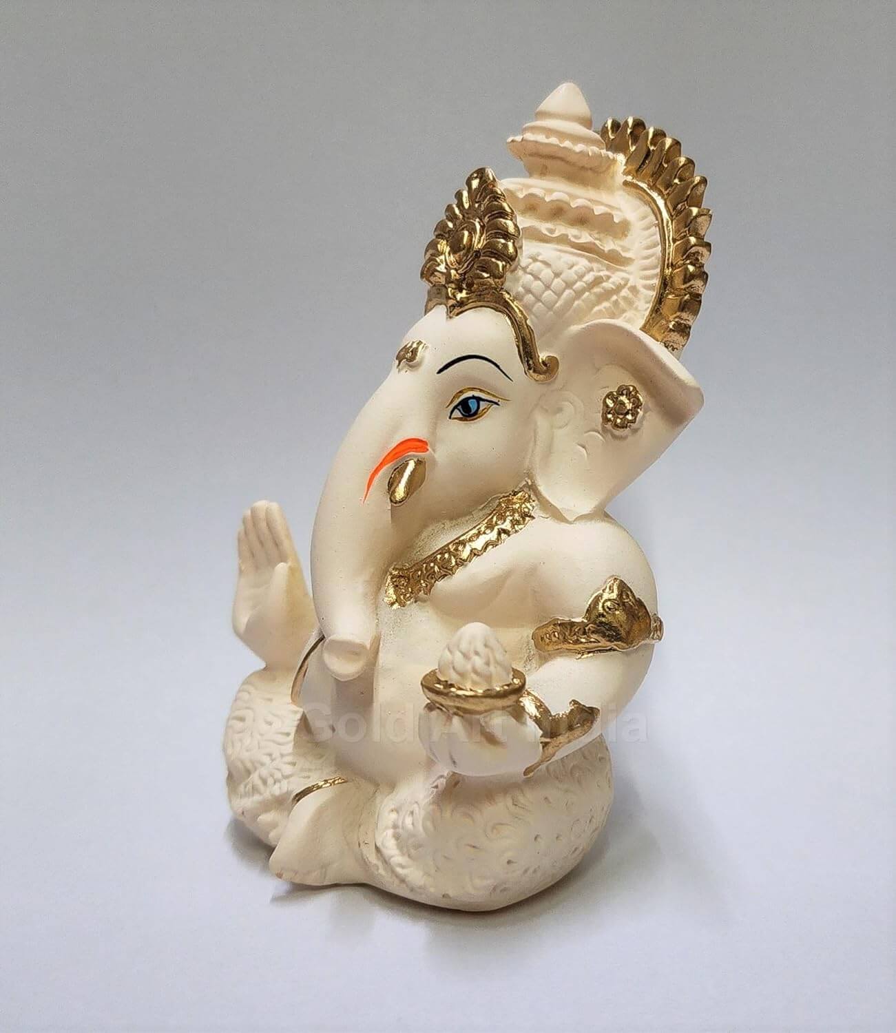 Peach ivory Lord Ganesha idol with intricate gold detailing, seated in a blessing posture, holding a modak in one hand.