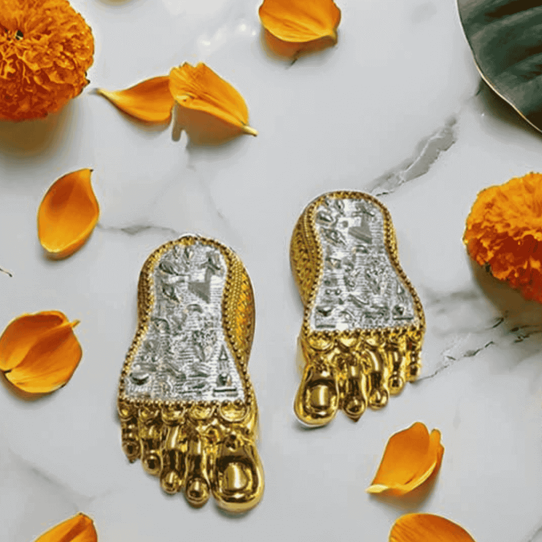 Shri Laxmi Charan Paduka gold and silver plated feet idol with flower petals on marble surface.