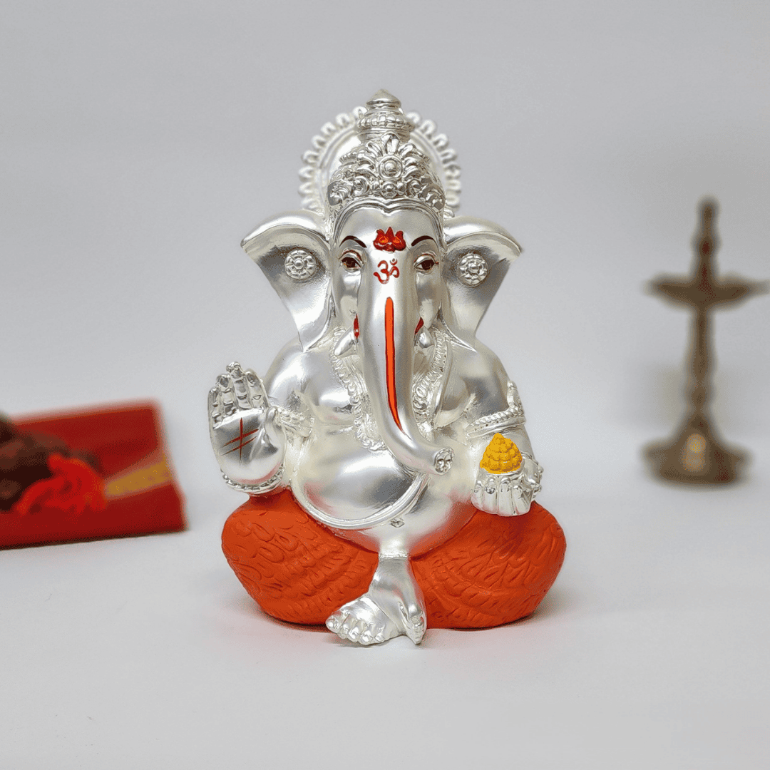 Silver Matte Mukut Ganesh Idol with orange dhoti and yellow ladoo, perfect for spiritual decor and gifts.