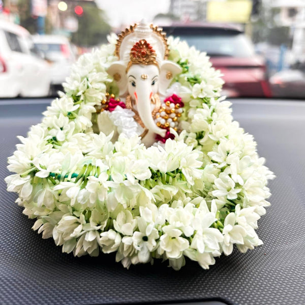 Gold and red-crowned Ganesha idol on car dashboard with white jasmine garland – symbol of divine protection and purity during travel