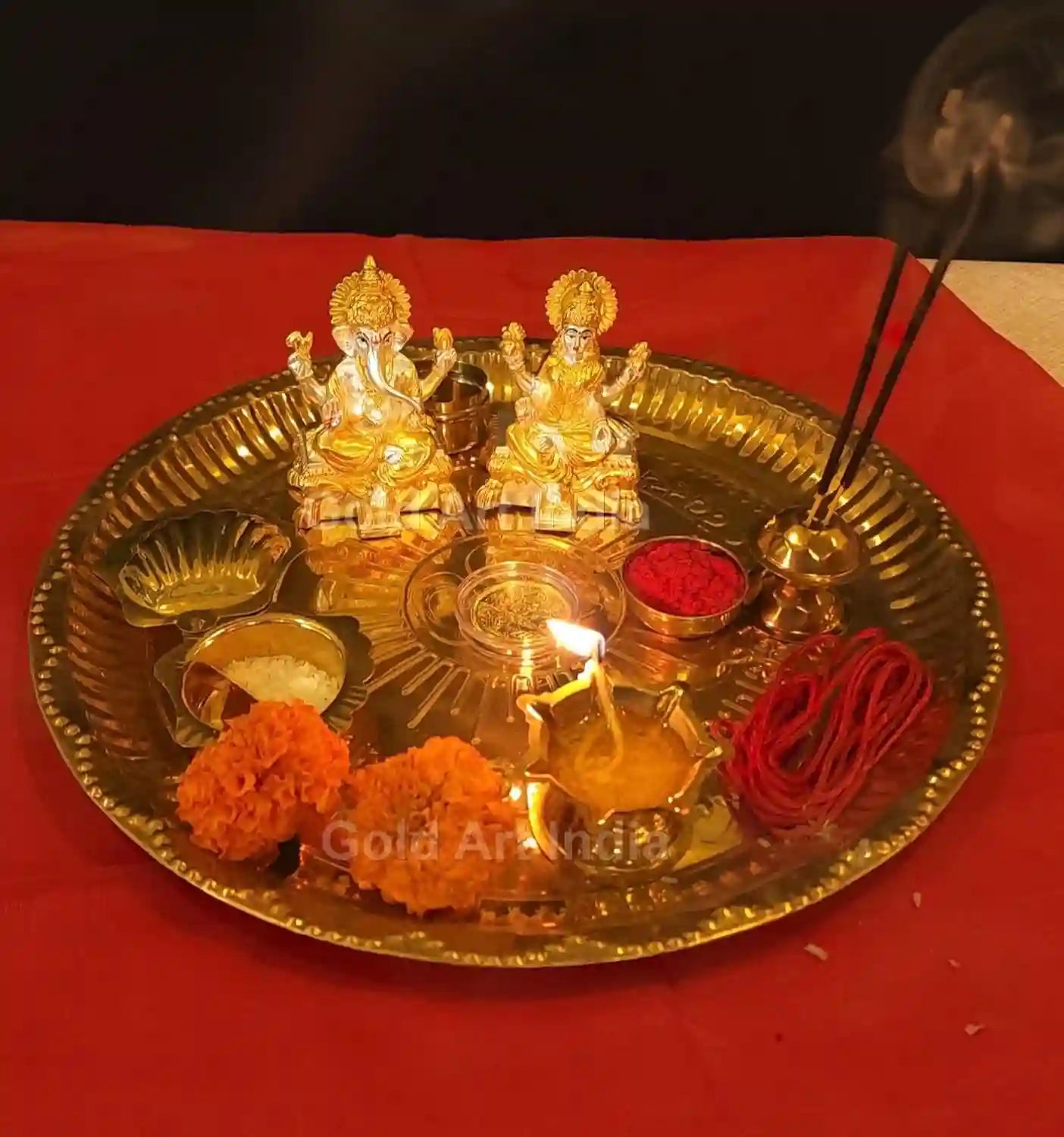 Gold and silver plated Lakshmi and Ganesha idol pair displayed with festive background including diyas and red cloth 