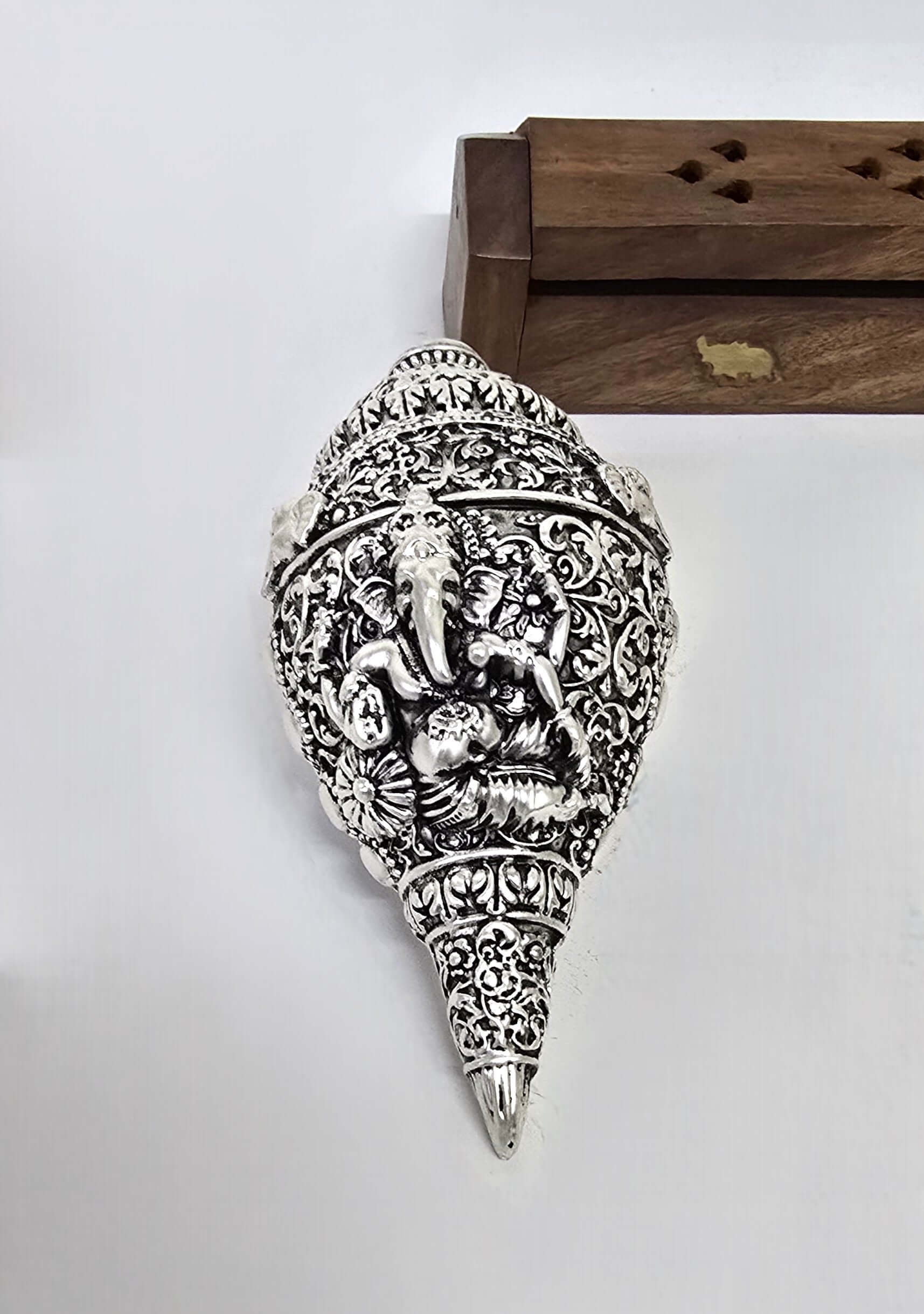 Silver-plated sacred conch shell (shankha) with an intricate carving of Lord Ganesha, held in hand for scale