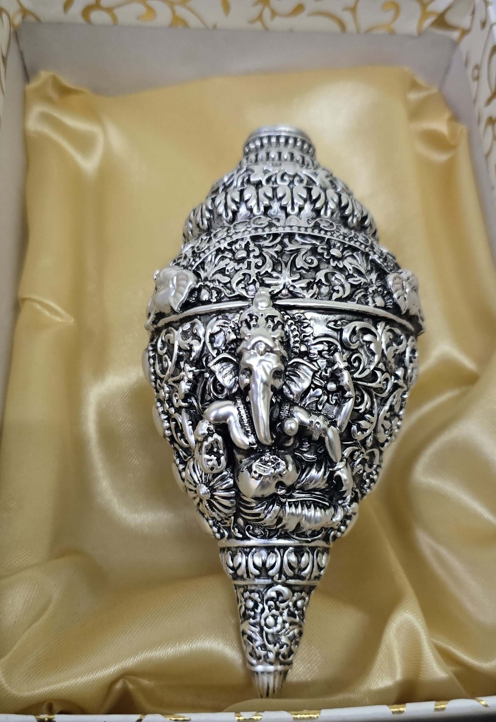 Ornate silver-plated conch shell (shankha) with a detailed carving of Lord Ganesha, presented in a golden satin-lined gift box