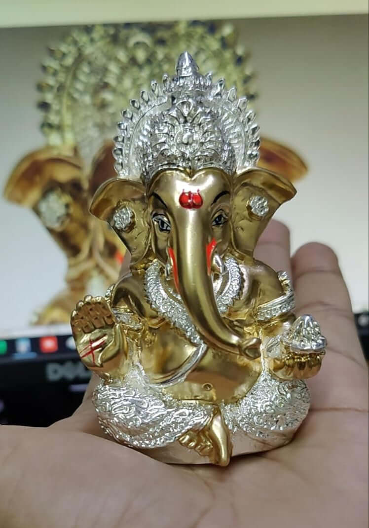 Silver Plated Antique Gold finish Ganesha idol with detailing, seated in a blessing posture, holding a modak in one hand.