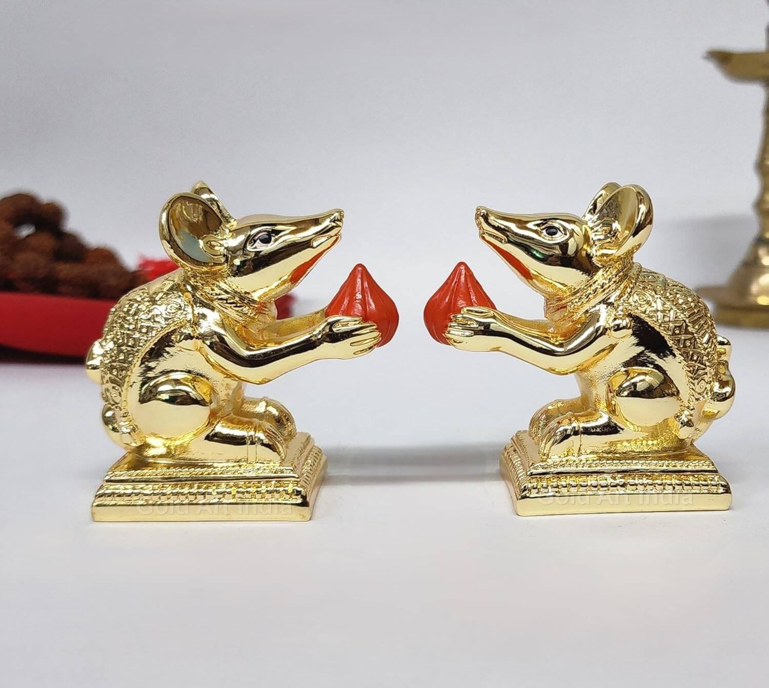 Gold-plated Mooshak mouse idol pair holding modaks, perfect for pooja space and spiritual decor.
