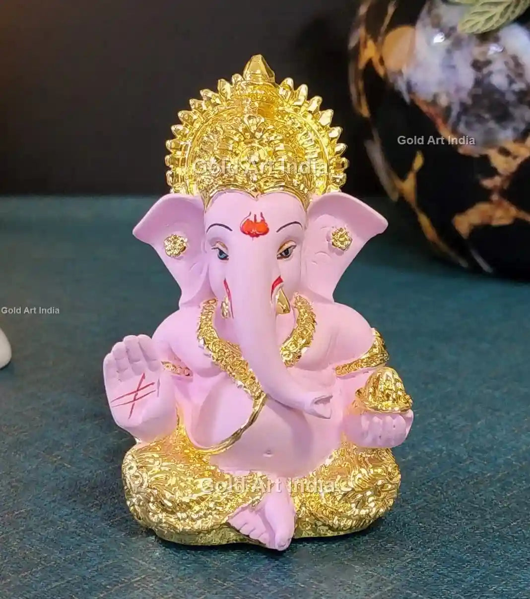 Front view of a white and gold Lord Ganesha idol with intricate detailing, a blessing hand, and a modak in the other.