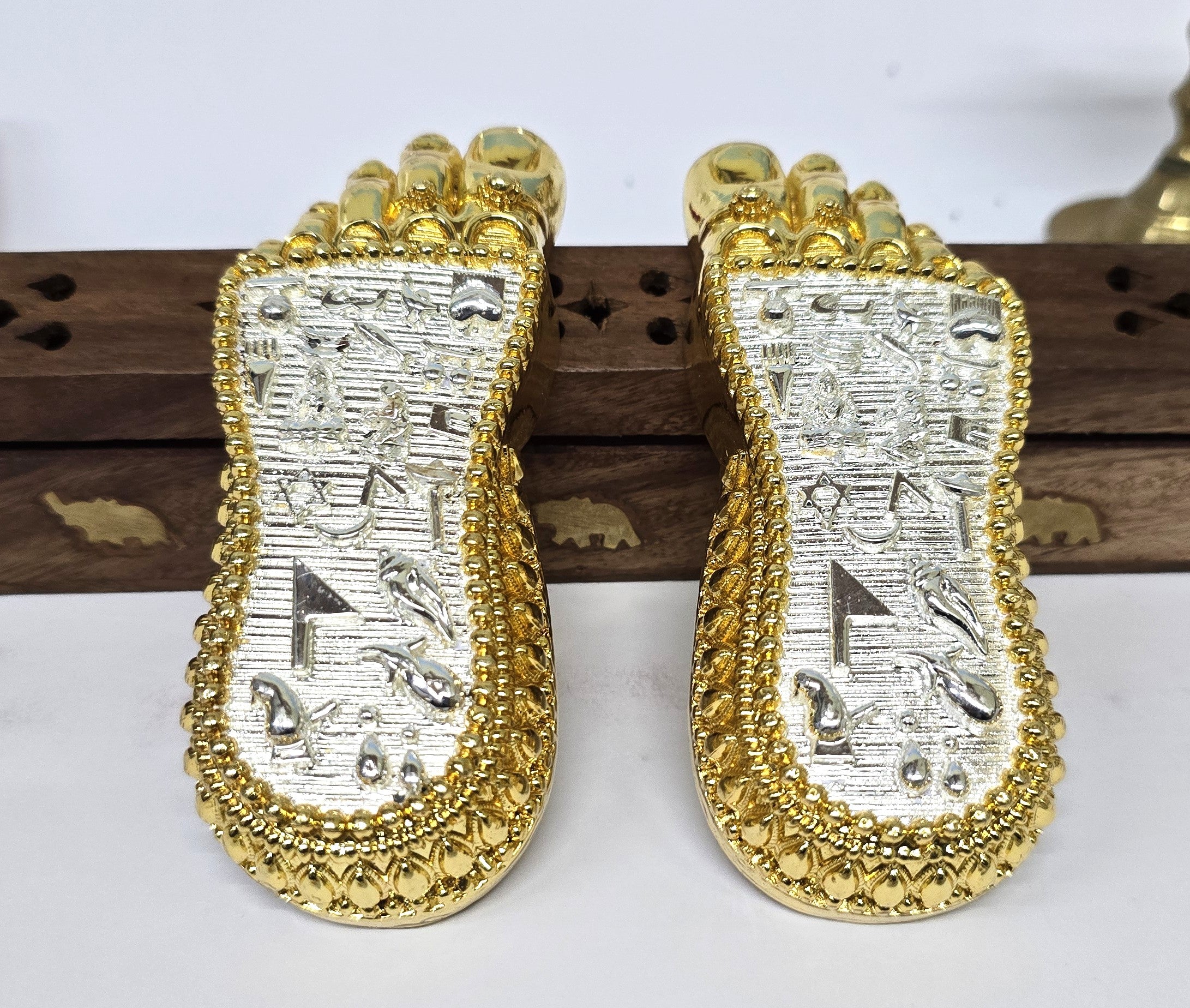 Angled view of gold and silver plated Charan Paduka showing embossed spiritual symbols and fine detailing.