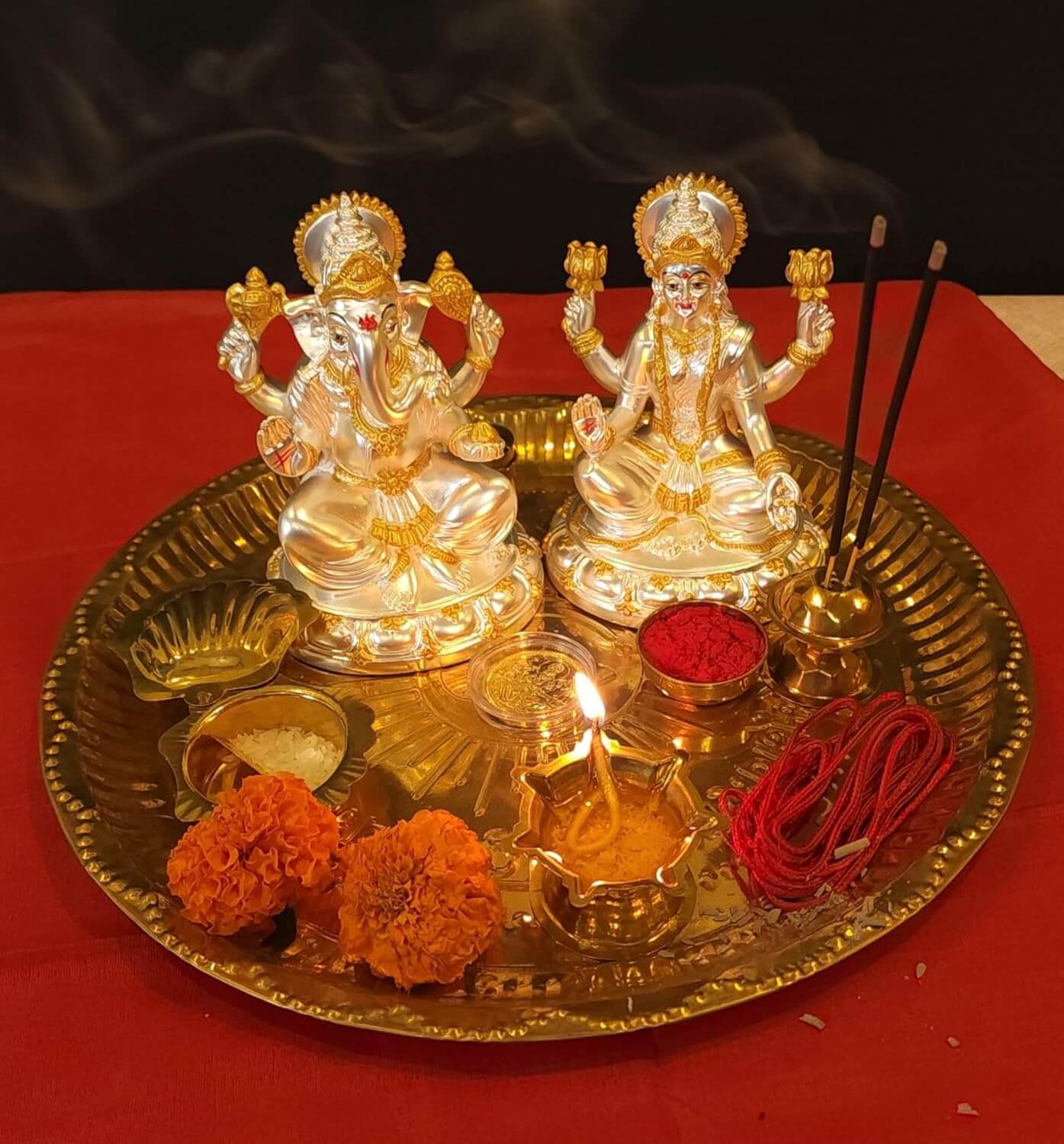 Silver plated Laxmi and Ganesha idols on a brass puja thali with flowers, incense sticks, and diya for Diwali.
