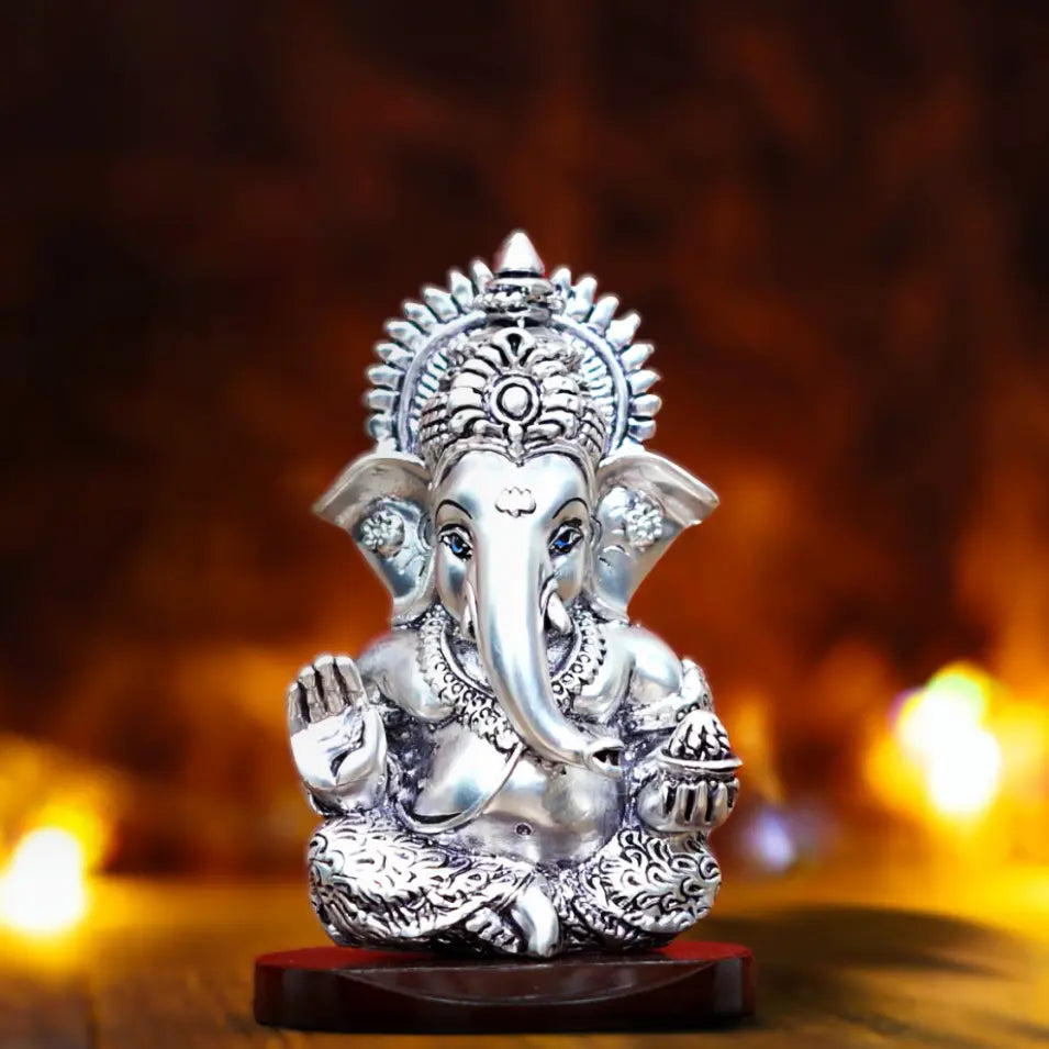 "Silver-plated Lord Ganesha idol with fine detailing, seated on a wooden base with festive lights in the background